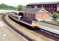 A class 47 drags a dead electric train south through Dumfries in June 1991. The now demolished ex-Caledonian goods depot dominates the background on the east side of the station.<br><br>[John Furnevel 23/06/1991]