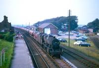 One of the 852 Stanier 8F 2-8-0s to be built, no 48033 of Sutton Oak shed, St Helens (8G), coasts south through Ravenglass station on the Cumbrian Coast with a lengthy freight circa 1966. The passing locomotive receives a greeting from a gathering of children (presumably part of a school trip) waiting on the northbound platform. The terminus of the adjacent Ravenglass & Eskdale Railway can be seen on the right.<br><br>[Robin Barbour Collection (Courtesy Bruce McCartney) //1966]