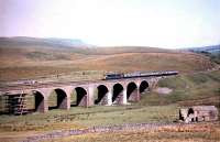 A class 47 brings a southbound train across Dandry Mire viaduct on the Settle & Carlisle line in 1984. The train is approaching Garsdale. The trackbed of the Hawes branch is visible in the lower left of the photograph and Wild Boar Fell stands on the skyline.<br><br>[Colin Alexander //1984]