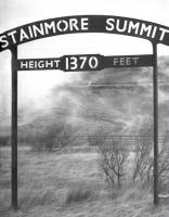 View from a train - 1962. Photograph taken from <I>The Stainmore Limited</I>, as 77003+76049 haul the 9 coach special over Stainmore summit, commemorating the end of operations on the line. The <I>South Durham and Lancashire Union Railway</I> route across the Pennines was notorious for snow blockages in winter with a summit height of 1,370 ft (compared with Shap at 914 ft and Beattock at 1,033 ft) placing it between Slochd (1315 ft) and Britain's highest main line summit at Druimuachdar (1484 ft). The old cast iron summit signs are now preserved, one at the NRM in York, the other at North Road Museum in Darlington.<br><br>[K A Gray 20/01/1962]