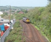 156449 is on the last part of its journey to the Harbour station at Stanraer and just about to swing into the shallow cutting that leads down to the breakwater. Directly above the train the roof of Stranraer steam shed can be seen over the trees [See image 15270] with the disused lines to Stranraer Town to the left.<br><br>[Mark Bartlett 23/05/2011]