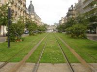 View north north west along Cours Jean-Baptiste Langlet of a scenic section of the light rail tram network that crosses Reims from north east to south west of the city. This city centre section does not use overhead catenary, instead appearing to use a mid track induction pick up arrangement to avoid marring views of Reims Cathedral, a short distance to the rear. Langlet tram stop is just beyond the van crossing the tracks ahead.  Immediately behind the camera is a temporarily closed section due to rebuilding of the area around the Opera tram stop on Place Myron T Herrick.<br><br>[David Pesterfield 24/07/2015]