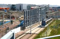 A tram heading for Edinburgh Airport runs west through the site of the under construction Edinburgh Gateway station on 7 June 2016. The bridge linking the rail and tram sides of the interchange has recently been installed. Edinburgh Gateway is scheduled to become operational by the end of 2016<br><br>[John Furnevel 07/06/2016]