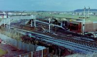 Looking northeast from the road bridge over Barassie Junction, Monday, 29 November, 1982, with the weekend's work by the PW and signalling engineers plain to see (well it would be if the photo was of better quality). Track-wise, the Kilmarnock line had been reduced to a single line (until that weekend, double track had extended round the curve onto the straight towards Drybridge before converged into single line to Kilmarnock, whilst a new crossover had been formed from the slewed 'up' (southbound) main line onto the old alignment of the same line, both 'Up' and 'Down' main lines slewed west starting from the platform ends approximately. The semaphore signals were in the process of being felled, their arms already removed, their replacements in the form of colour lights just about visible beyond the footbridges (that over the Kilmarnock lines was removed along with the signals, whilst the other section over the line to Irvine survived until electrification saw it replaced, circa 1985. The temporary Signalbox, officially opened that day, is the brick-built structure on the east side of the line between the footbridge and the remains of the Kilmarnock line bracket signal. <br><br>[Robert Blane 29/10/1982]