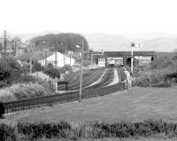 Looking north east  towards Millom station on the Cumbrian Coast line in October 1983 just as a Carlisle – Barrow DMU pulls into platform 1 on the other side of St George's Road bridge. Several sidings still in existence around the station at this time had been associated with the former Millom Ironworks, which closed in 1968 [see image 26680]. <br><br>[John Furnevel 07/10/1983]