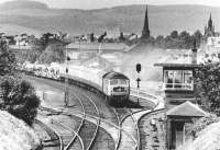 The Perth - Kensington Olympia Motorail service starts to pick up after passing through Dumfries station in April 1971 and is about to run past Dumfries South box. View is north west towards the town centre, with the distinctive outline of St Mary's parish church on the extreme right of the picture.<br><br>[John Furnevel 08/04/1971]